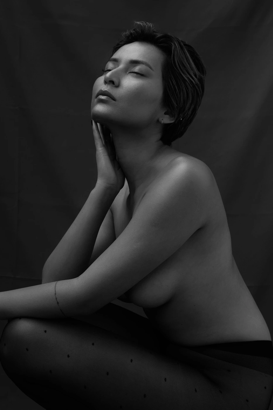Black and white portrait of a woman with short hair crouching with her hand touching her cheek, photographed by Ruby Watt.