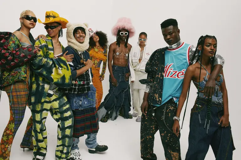 Group of eight diverse models in eclectic streetwear fashion, posing indoors against a white backdrop, showcasing unique textures and designs.