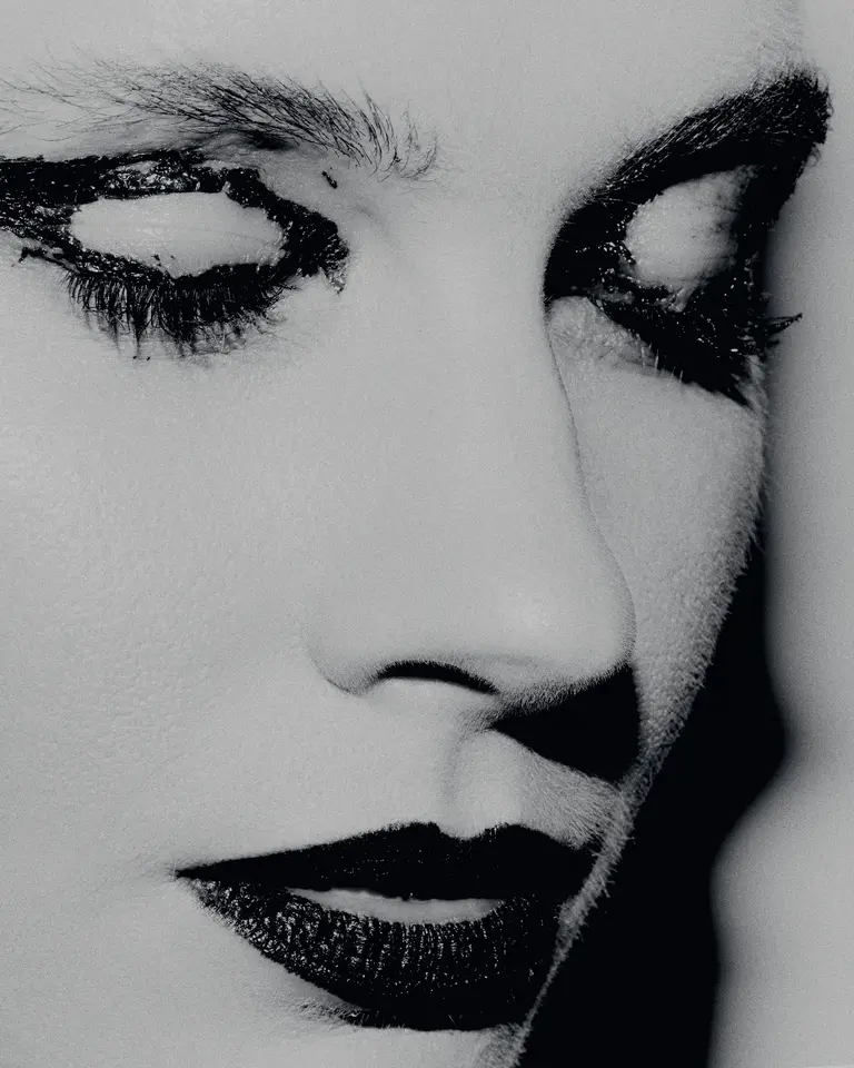 Monochrome portrait of a person with dramatic dark makeup around the eyes and lips, with soft lighting highlighting facial features.
