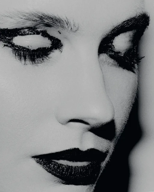 Monochrome portrait of a person with dramatic dark makeup around the eyes and lips, with soft lighting highlighting facial features.
