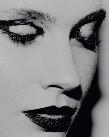 Monochrome portrait of a person with dramatic dark makeup around the eyes and lips, with soft lighting highlighting facial features.