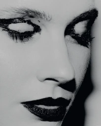 Close-up portrait of a woman with dramatic black eye makeup and dark lipstick in a monochrome aesthetic.
