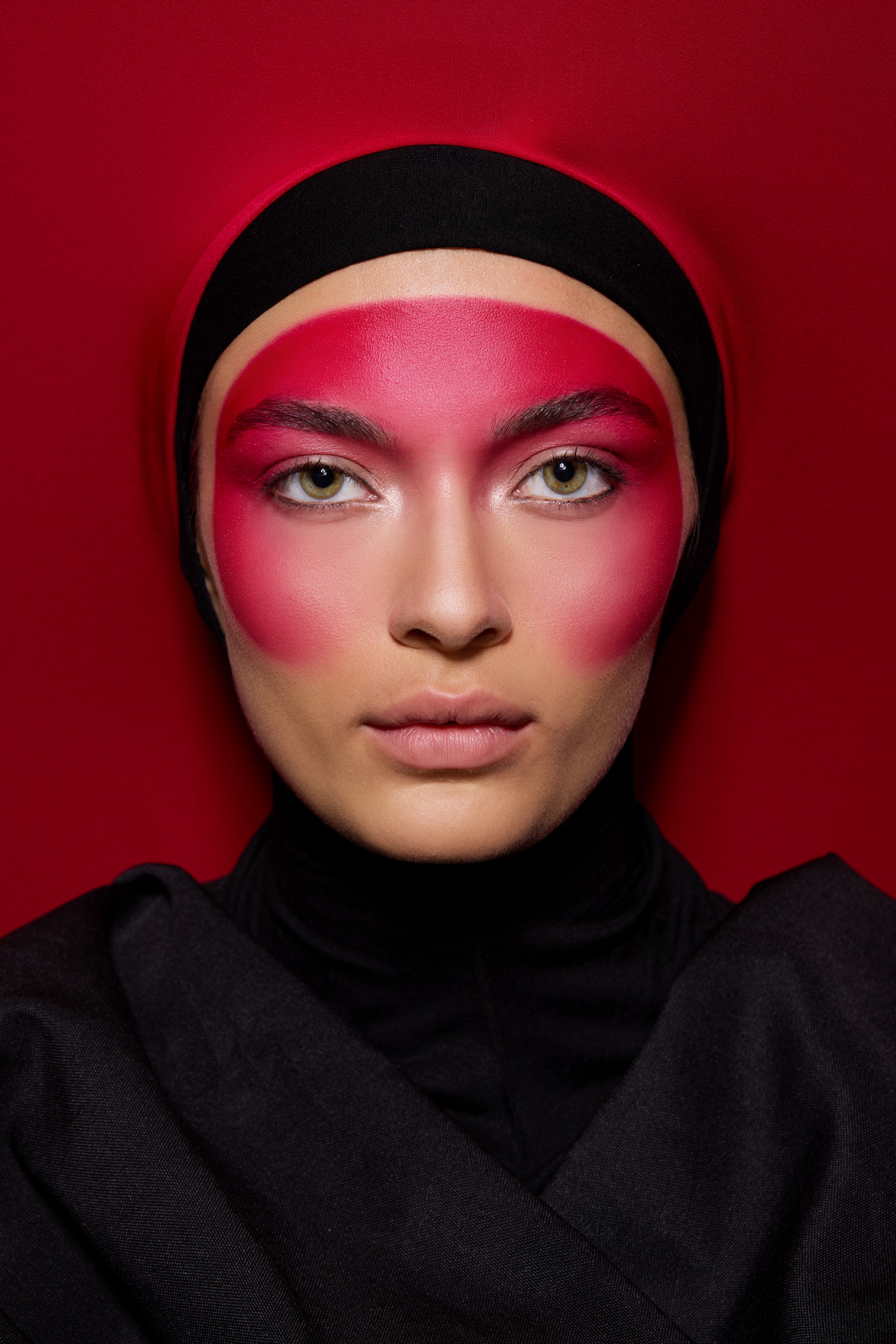 Close-up studio portrait of a woman with vibrant red face paint and a black head covering, set against a matching red backdrop.
