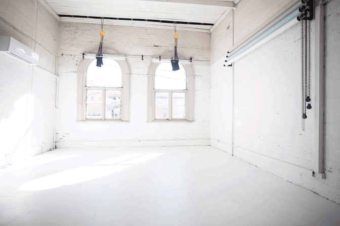Empty white photo studio with natural light from windows and suspended equipment in the ceiling.