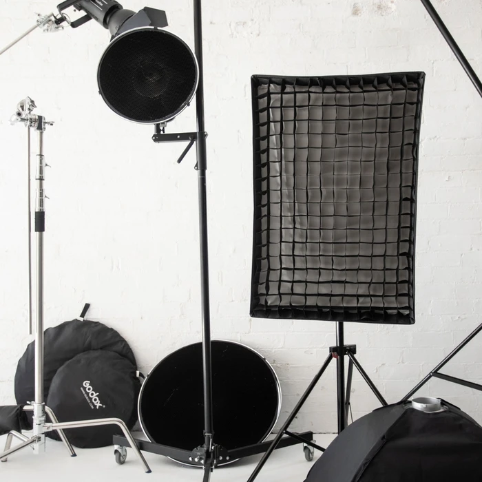Professional photography studio equipment including studio lights, softboxes, stands, and reflectors against a white brick wall.