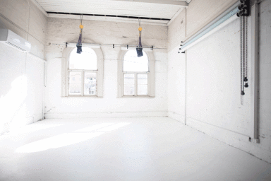 Bright, empty white photo studio interior with arched windows, high ceilings, and mounted backdrop roll chains in Sydney.