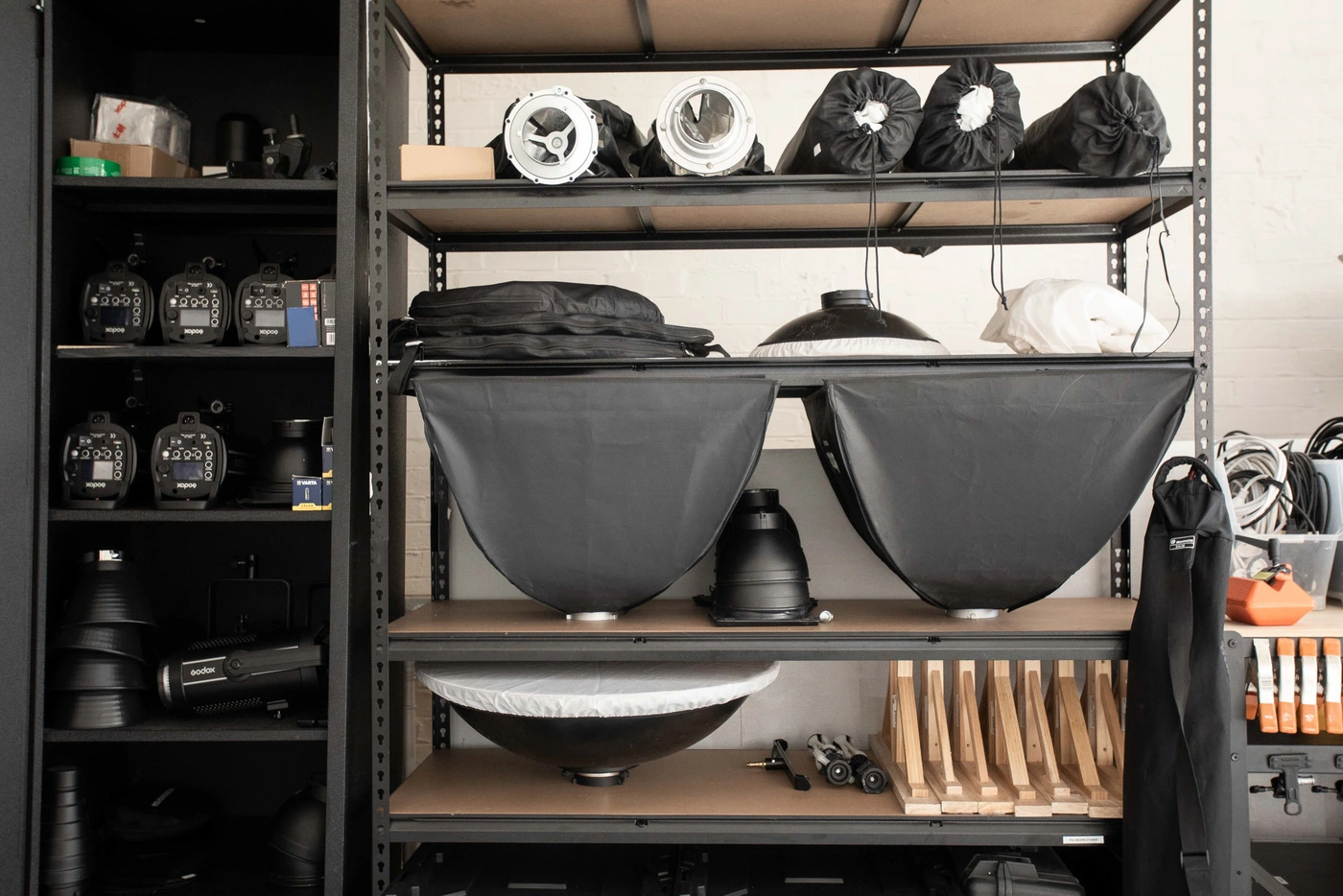 Black metal shelving unit organized with photography studio equipment, lighting modifiers, and cases in Sydney by Desk and Studio