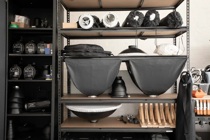 Black metal shelving unit organized with photography studio equipment, lighting modifiers, and cases in Sydney by Desk and Studio
