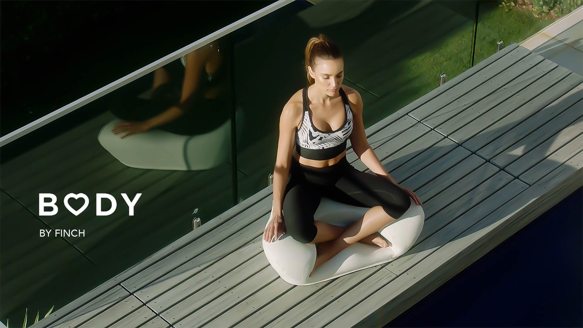 Adult woman in athletic wear sits cross-legged on an outdoor patio for a fitness shoot, bathed in natural light, promoting health.