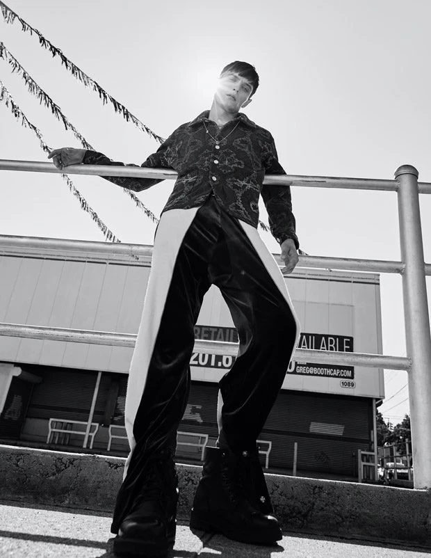 Low angle monochrome fashion portrait of a male model leaning against a metal railing outdoors in bright daylight