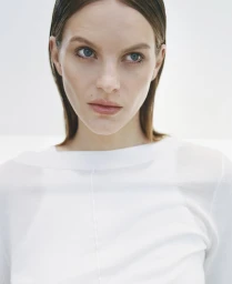 Close up portrait of a woman with slicked back brown hair wearing a white top against a clean white background