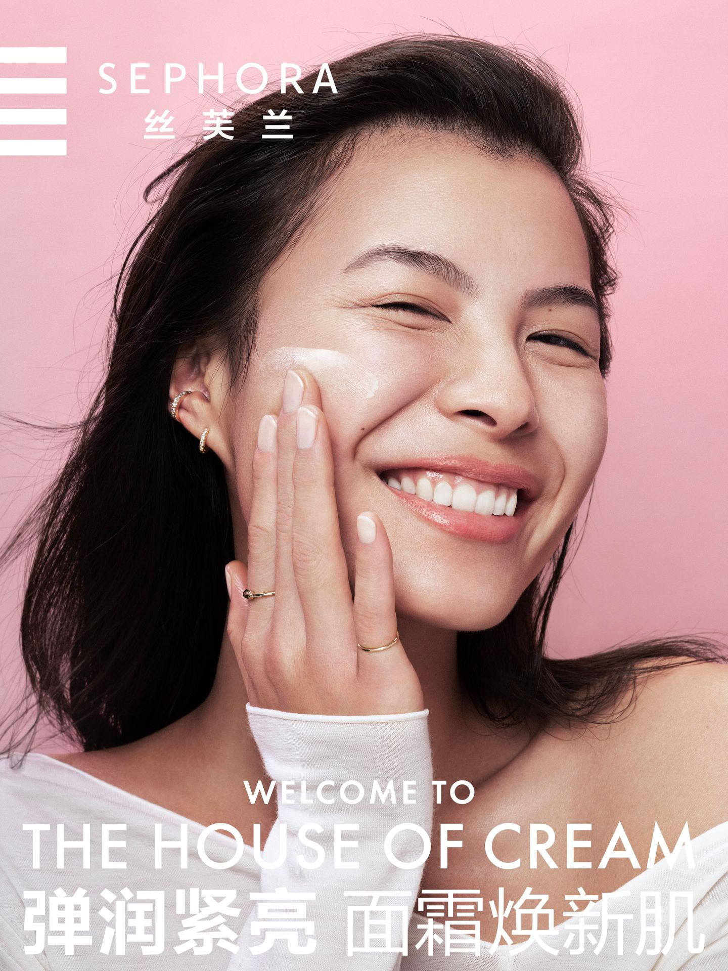 Asian woman with cream on her face smiling in beauty shot for Sephora.  She's wearing a long-sleeved white shirt against a pink background.