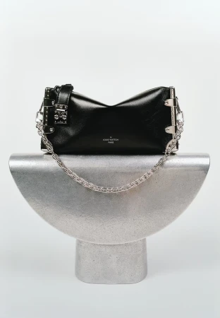 Black leather Louis Vuitton handbag with metal hardware and silver chain strap displayed on a silver metal stand against a white backdrop.