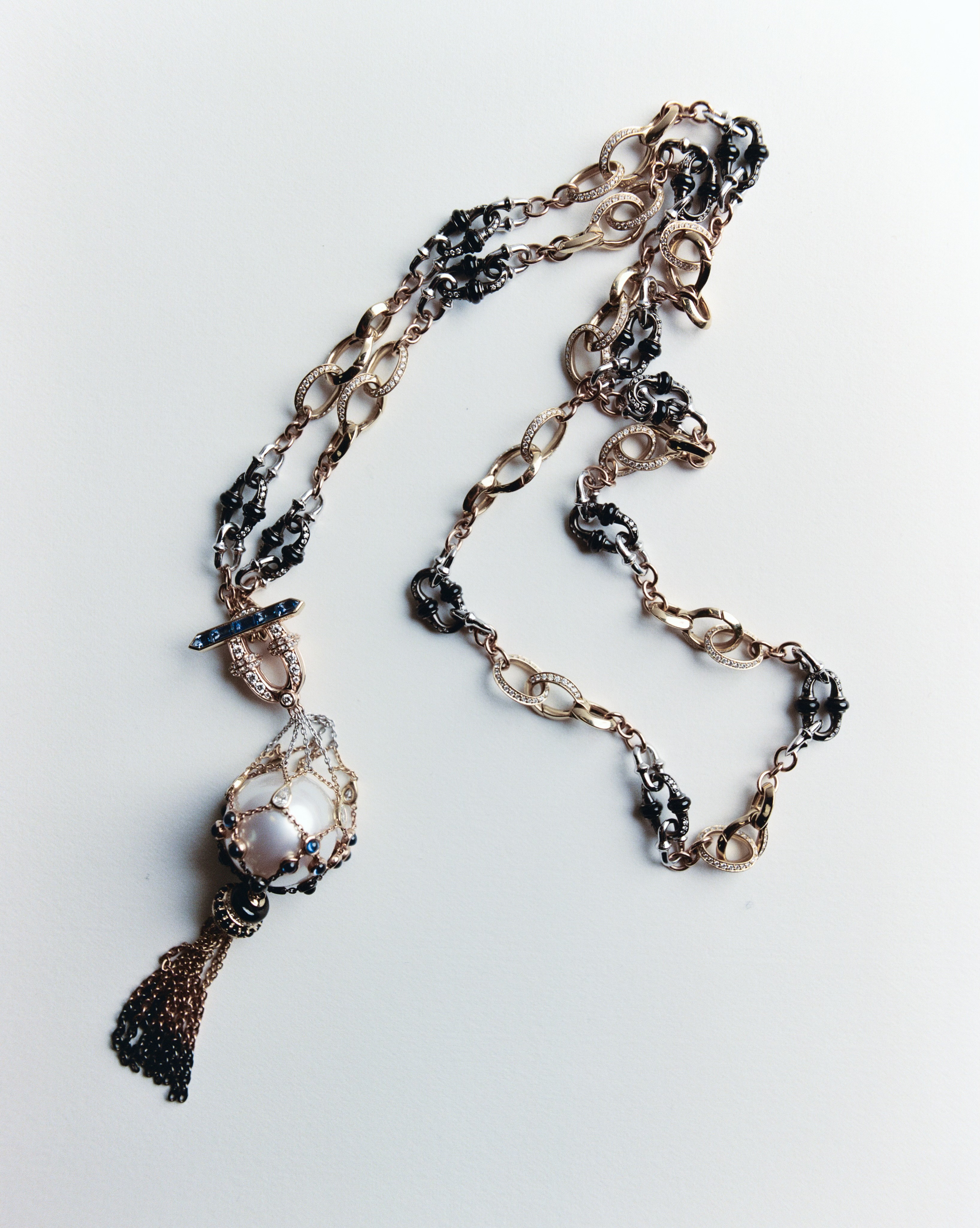 Elegant long necklace featuring gold and black chains, a large pearl, and a tassel, displayed on a clean white background.