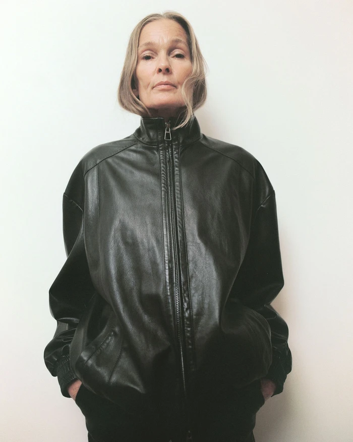 Mature woman wearing a black leather zip-up jacket against a plain white background