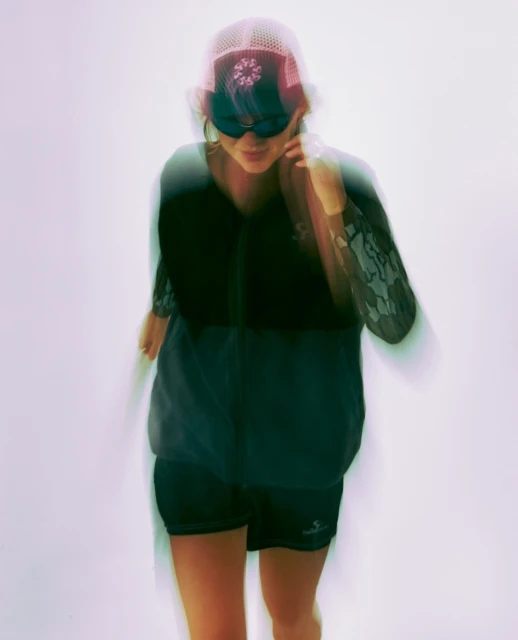 Woman in sunglasses and athletic wear in motion against a white background with long exposure creates a blurred effect in a studio setting.