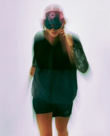 Woman in sunglasses and athletic wear in motion against a white background with long exposure creates a blurred effect in a studio setting.