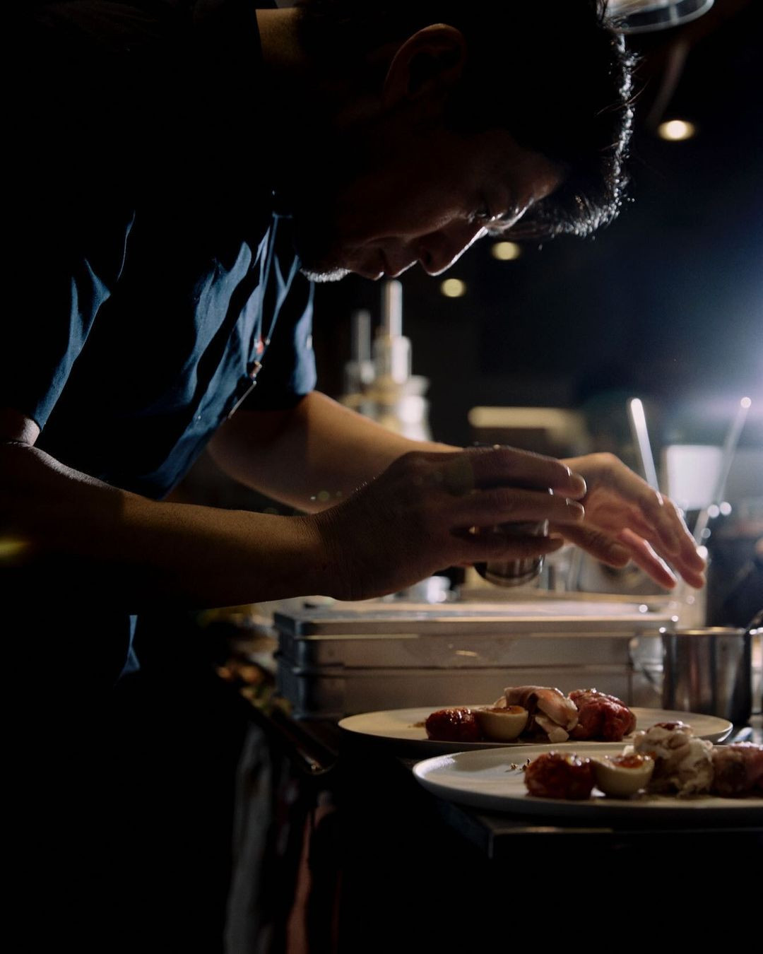Chef preparing food in restaurant. An adult male is shown plating food on plates, working in a dimly lit commercial kitchen setting.