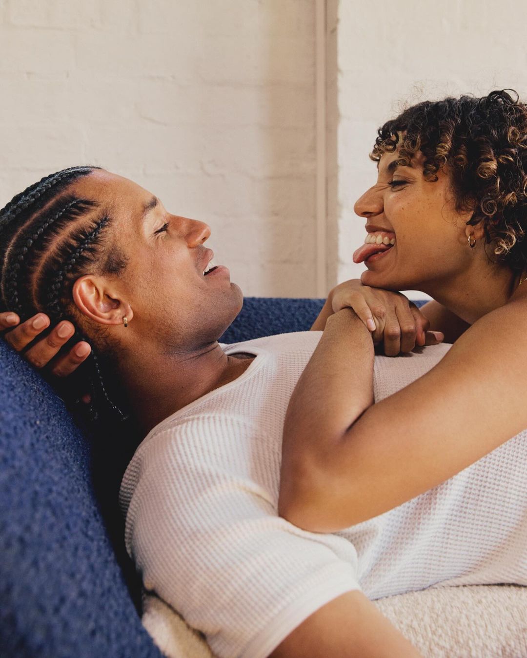 Close-up portrait of a man and woman smiling and laughing together on a blue sofa in a bright room.