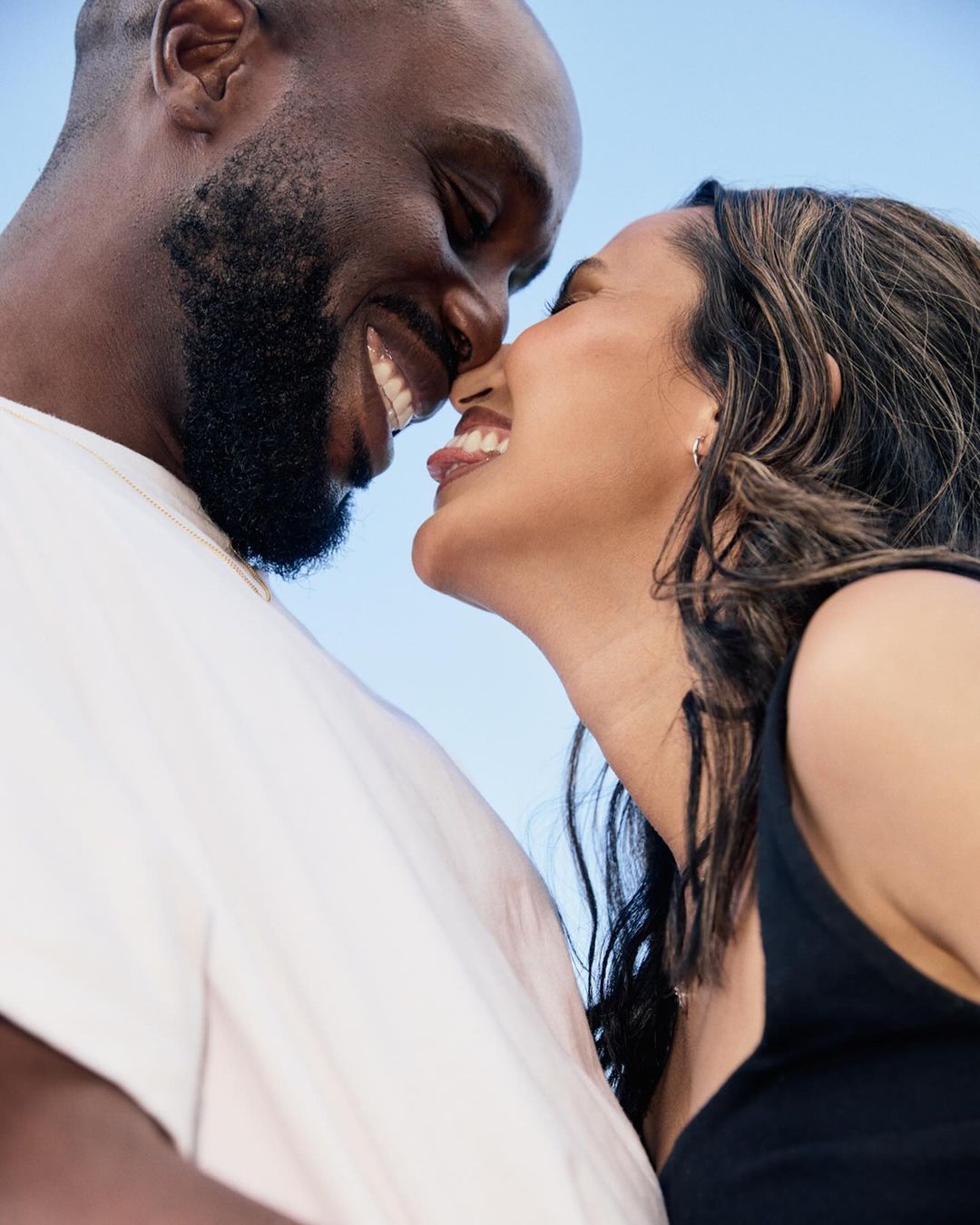 Close-up shot of a happy African American couple, face to face, with bright light blue background. Both smiling, dressed in casual clothes.