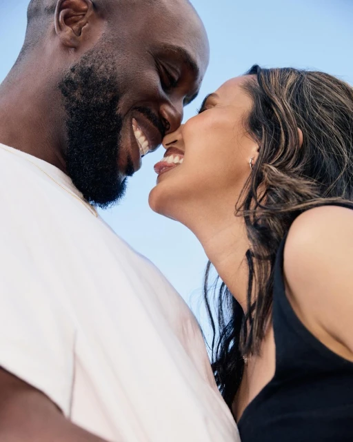 Close-up shot of a happy African American couple, face to face, with bright light blue background. Both smiling, dressed in casual clothes.