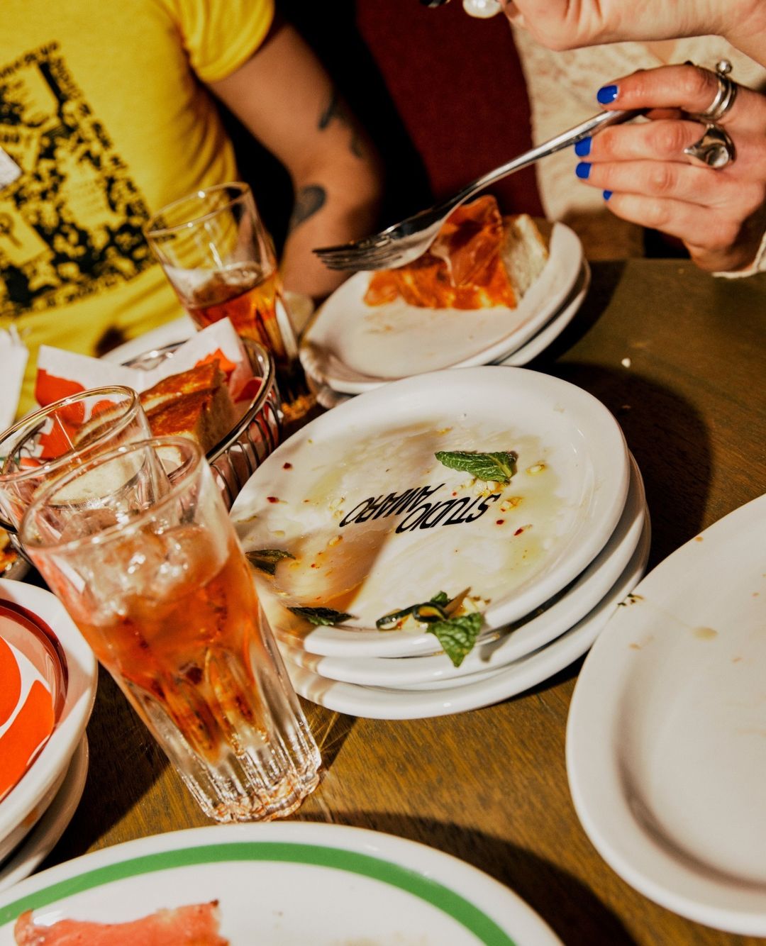 Close-up of a table setting with dirty plates and glasses, featuring leftover food, cutlery, and beverage remnants, in warm lighting.