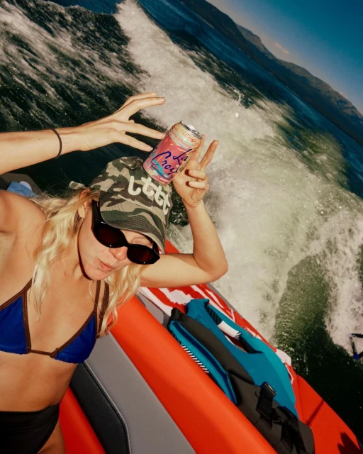 Woman in bikini balancing a La Croix beverage can on her head with crashing waves and blue water in the background on a sunny day.
