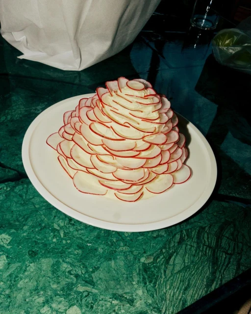 Radish and cream cheese appetizer on a white plate, set on a green marble table. The food is styled in a conical stack.