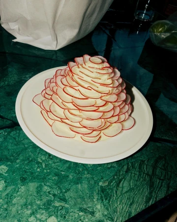 Radish and cream cheese appetizer on a white plate, set on a green marble table. The food is styled in a conical stack.