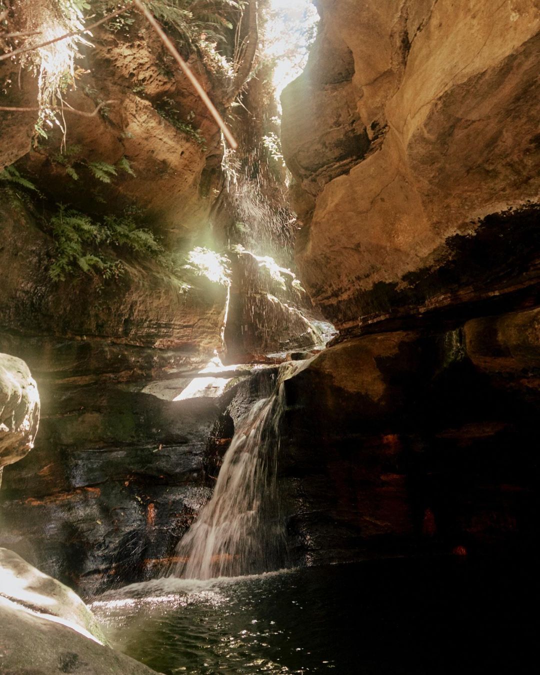 Waterfall cascading down rocks into a pool of water in a cave, highlighting nature's beauty with rock textures and light play.