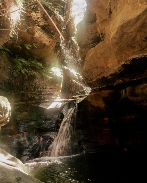Waterfall cascading down rocks into a pool of water in a cave, highlighting nature's beauty with rock textures and light play.
