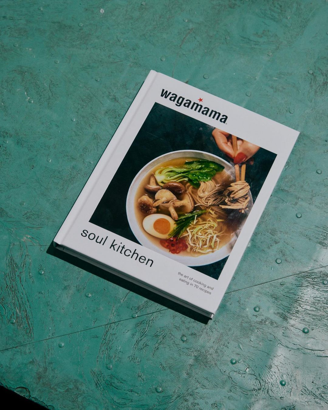 Wagamama cookbook, 'Soul Kitchen', features a bowl of ramen noodles with egg, greens, and mushrooms on a textured green surface.