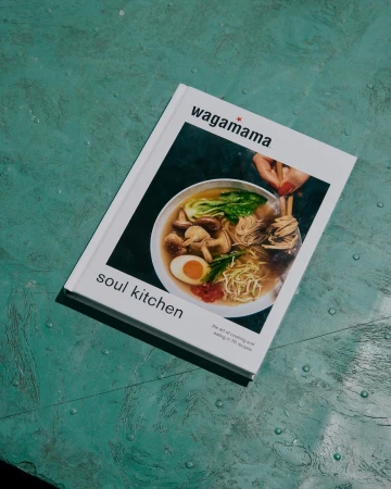 Wagamama cookbook, 'Soul Kitchen', features a bowl of ramen noodles with egg, greens, and mushrooms on a textured green surface.