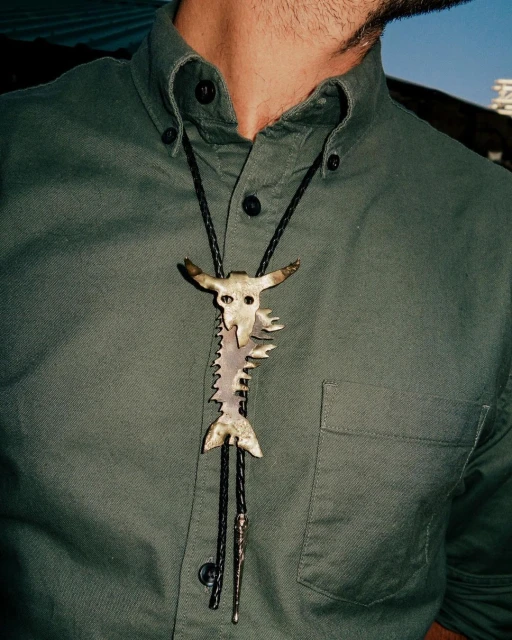 Adult male wearing a green button-down shirt and a metal bolo tie with a steer skull and fishbone design, close-up shot.