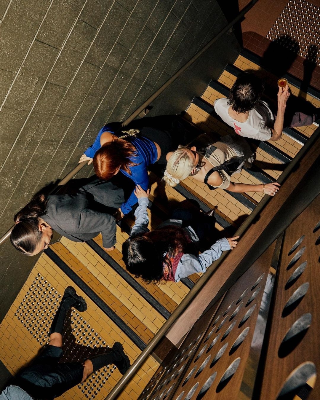 Overhead shot of six people on staircase in fashionably casual clothing, ranging from suits to blouses and t-shirts, indoors.