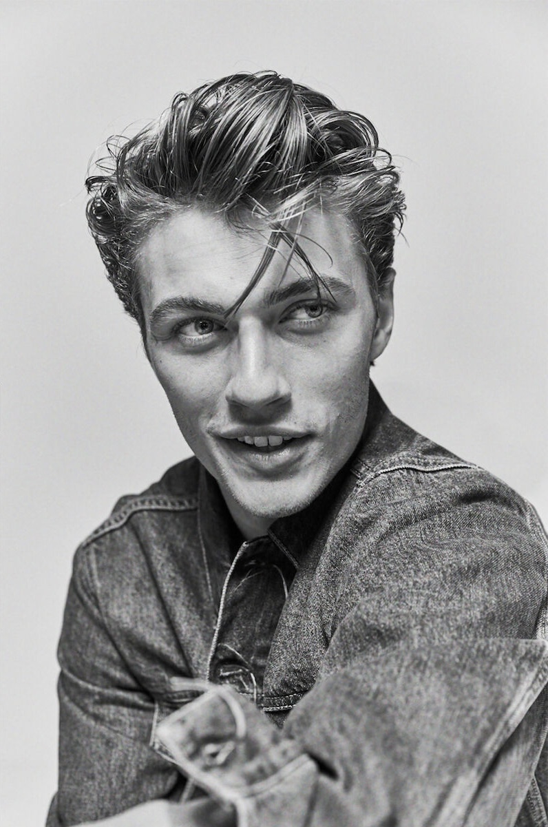 Portrait of a handsome young man with wet-look hair wearing a denim jacket against a neutral background in a studio setting.