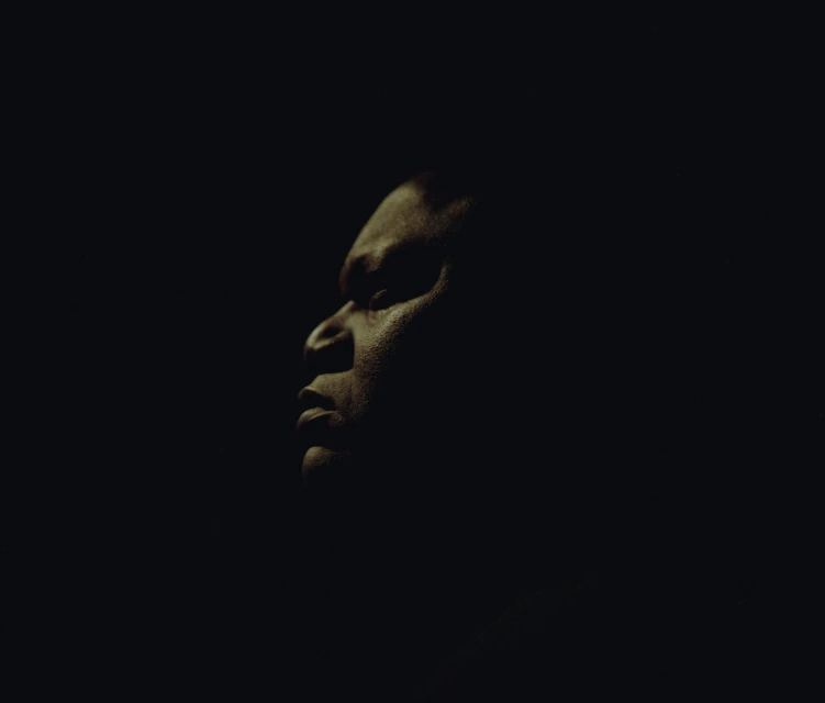 Close-up portrait of an African American man looking to the side in dark lighting, showcasing his profile and facial features.