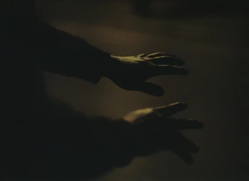 Close-up of two silhouetted hands hovering in low light against a dark, indistinct background.