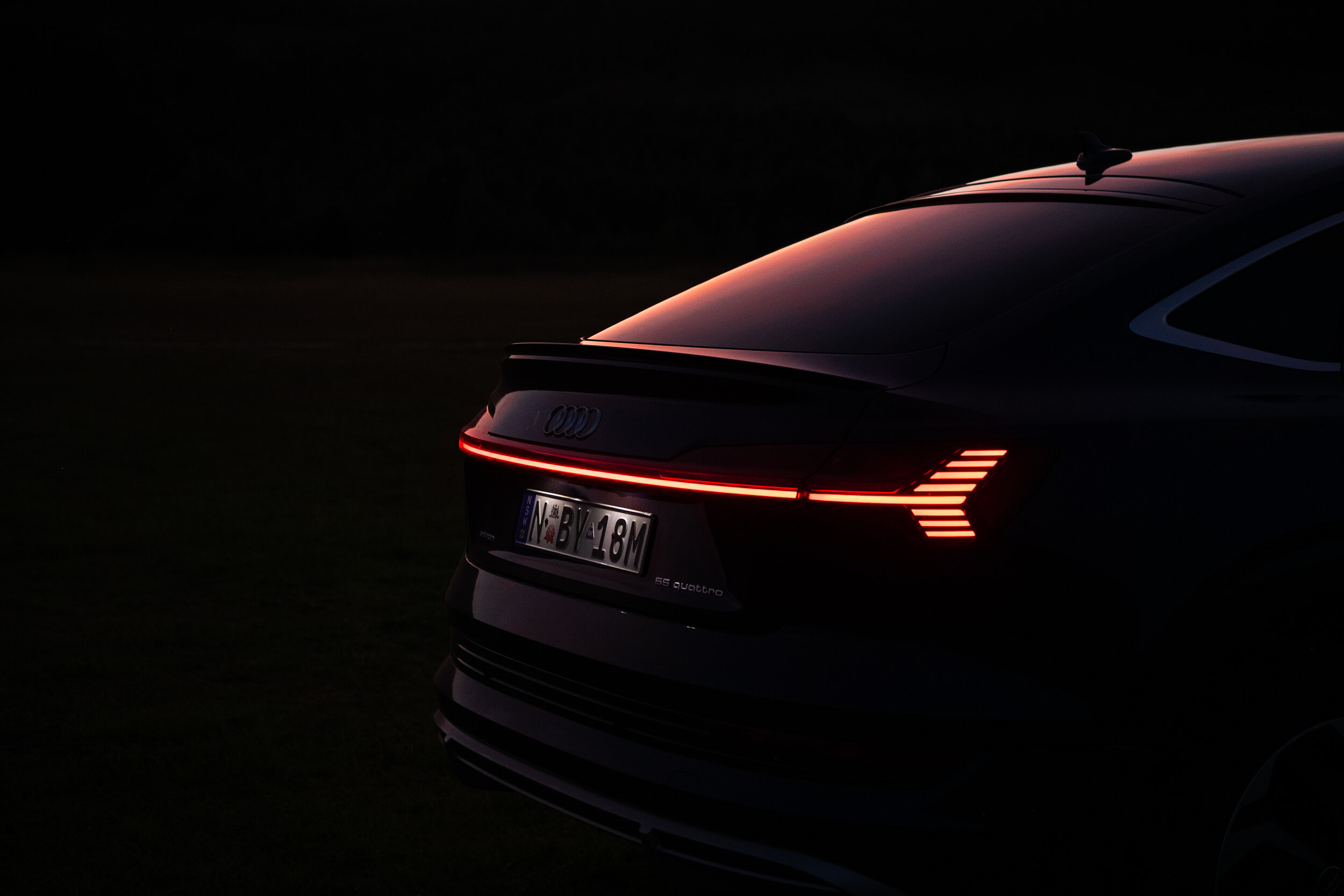 Rear view of a dark-colored Audi e-tron featuring a sleek design with distinctive horizontal and arrow-shaped lights during twilight.