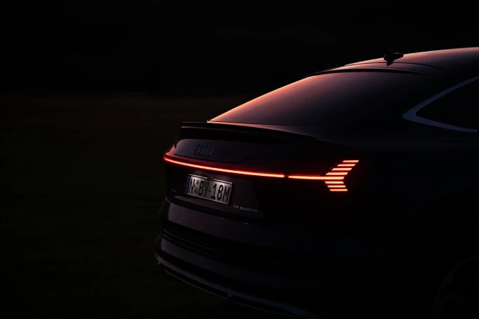 Rear view of a dark-colored Audi e-tron featuring a sleek design with distinctive horizontal and arrow-shaped lights during twilight.