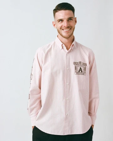 Handsome man in a light pink striped dress shirt with an architectural design and the letter 'A'. Smiling indoors against a white backdrop.