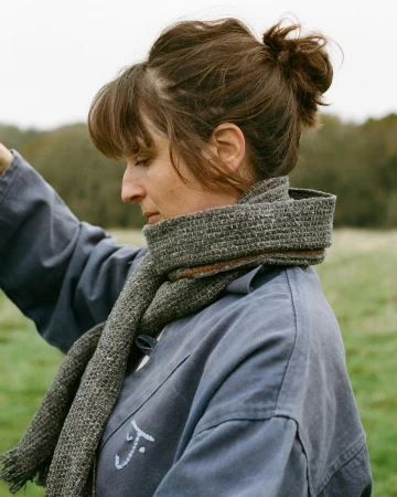 Portrait of a woman wearing a grey tweed scarf and blue jacket with a messy hair bun outdoors in Paris.