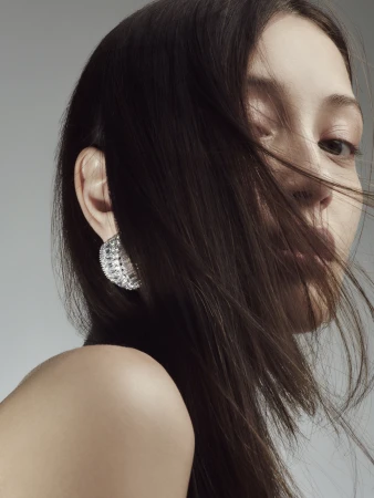 Close-up portrait of a woman with dark hair blowing across her face and wearing a textured silver hoop earring.