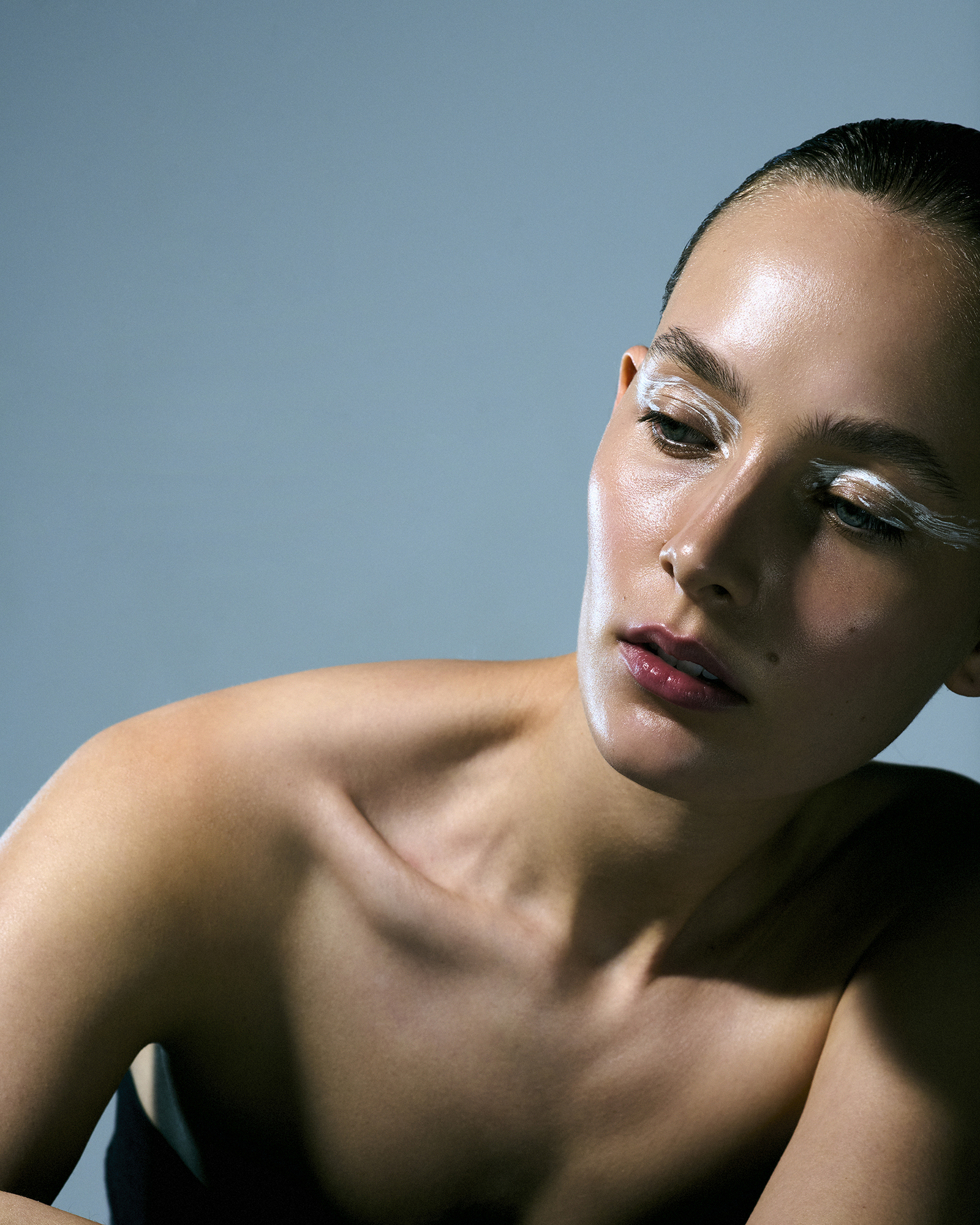 Close-up of a woman with fair skin and exaggerated white makeup on her lashes and brows against a solid blue background.
