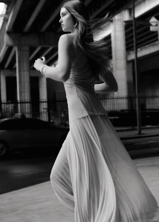Monochrome fashion shot of a woman in a flowing dress running beneath an overpass, captured in a medium shot with diffused lighting.