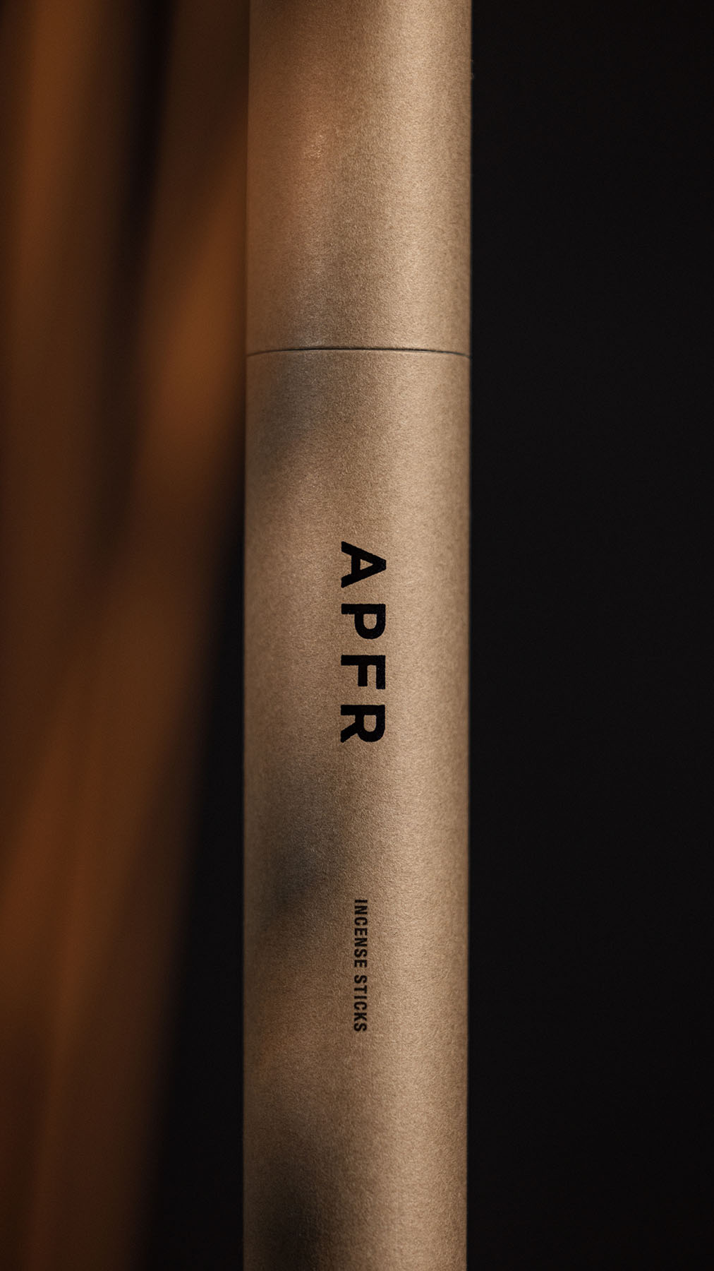 Craft-toned cardboard tube package with 'APFR Incense Sticks' text against a blurred dark backdrop for an organic, minimalist aesthetic.