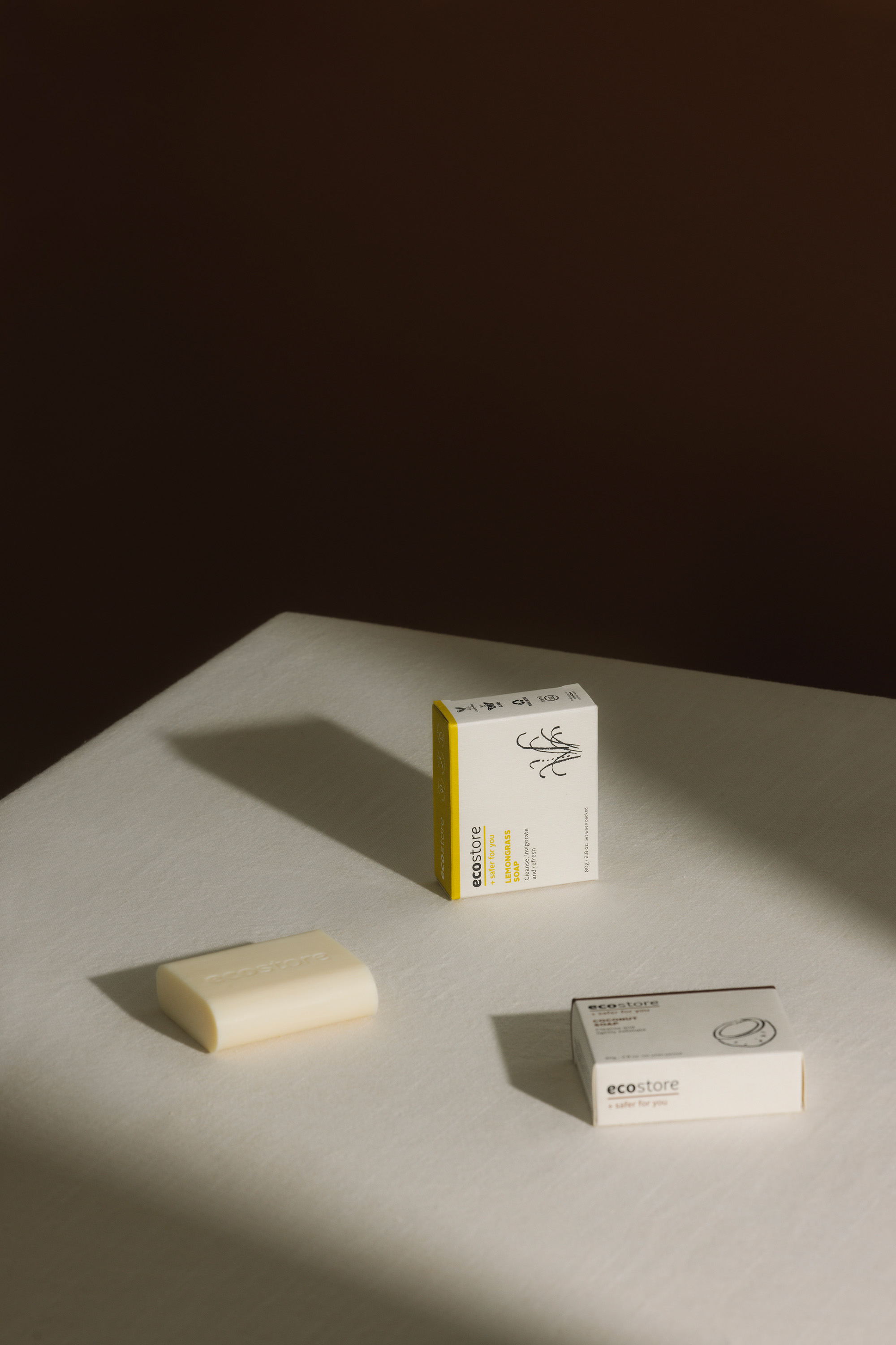 Still life shot of three ecostore-brand soap products, including a wrapped soap bar and two boxed soap products on a white surface.