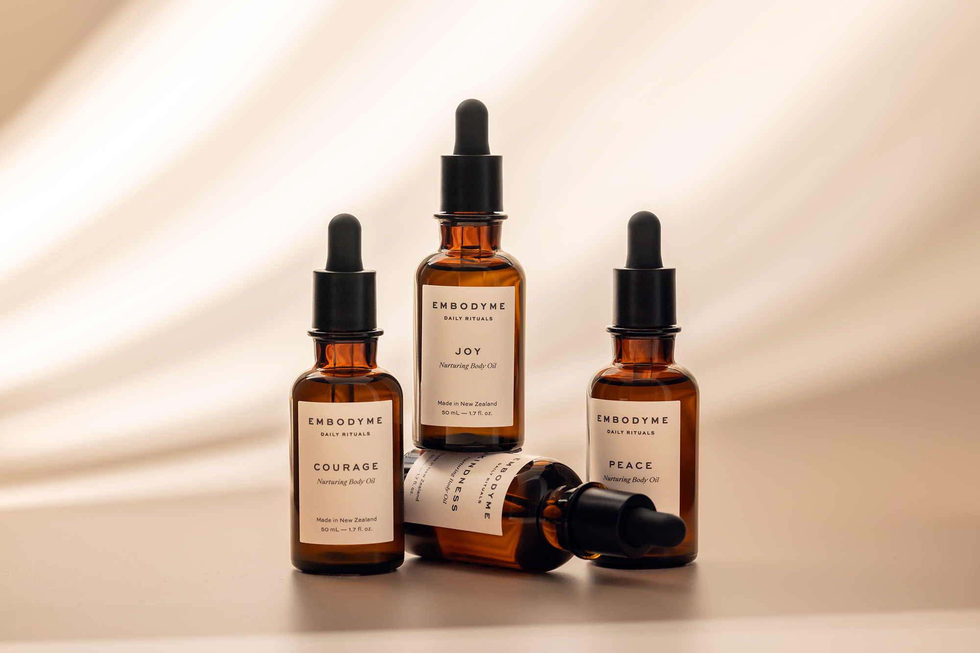 Amber glass bottles with black dropper tops arranged on a beige surface in a beauty and wellness product shot. Studio lit.