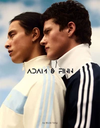 Two young men in athletic zip-up track jackets posing outdoors against a clear blue sky in Melbourne.