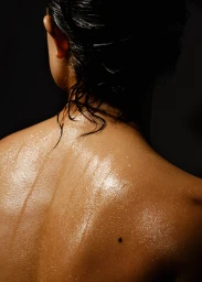 Close-up portrait of a person's wet shoulders and back against a dark background, photographed by Bryan Tang